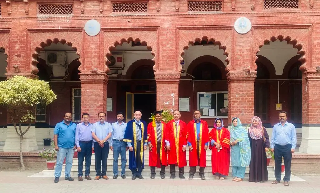 Dr. Muhammad Ihsan Ullah, Founder and Lead Content Writer, posing with the Principal of Punjab University College of Pharmacy, PhD supervisor, and two external examiners after his PhD defense at the University of the Punjab, Lahore, Pakistan. The group stands in front of the university’s historic red-brick building, with faculty members wearing academic gowns and formal attire.
